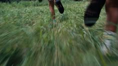 two people are running through the grass with their shoes on and one person is holding an umbrella