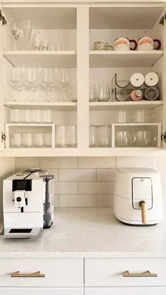 a kitchen with white cupboards filled with dishes and cups on top of it,