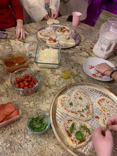 several people are making pizzas at a table with plates and bowls on the table