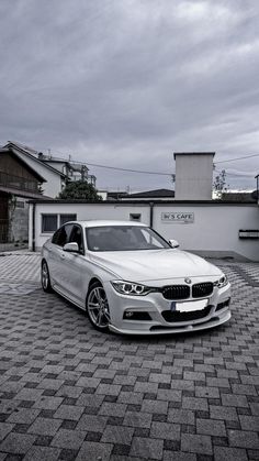 a white car parked in front of a building on a cobblestone driveway with the door open