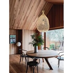 a dining room table with chairs and a vase on top of it in front of a wooden wall