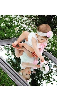 a baby sitting on top of a wooden bench in front of a mirror with flowers