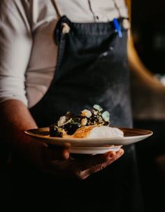 a person in an apron holding a plate with food on it and utensils