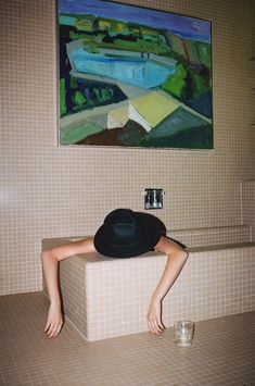 a woman in a black hat is sitting on a bathtub next to a painting