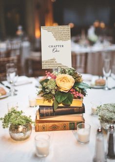 a table topped with books covered in flowers and greenery next to glasses filled with candles