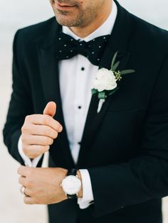 a man in a tuxedo with a watch on his left hand and a rose boutonniere on his right wrist