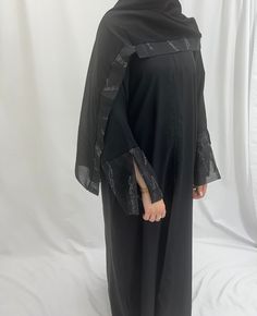 This elegant black open abaya is a stylish twist on classic black abayas with its dainty glittering embellishments. This unique abaya  has been design by our team and Looks effortlessly elegant: Perfect for day-long wear thanks to its smart, simple design and comfortable fabric as well as show-stopping occasion wear with its embellished piping, our black abaya is a year-round favourite for day and night. Matching  hijab included  Fabric Nidha   A 2 pieces abaya set  Abaya  Embellished Hijab  Lux Black Abaya For Eid Party, Black Party Abaya For Eid, Modest Black Kaftan For Eid, Black Maxi Length Kaftan With Dabka, Black Abaya With Dabka For Party, Long Black Abaya For Eid, Black Long Khimar For Eid, Black Long Sleeve Khimar With Dabka, Party Black Abaya With Dabka Detail