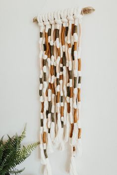 a wall hanging made out of white and brown yarn with tassels on it