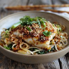 a white bowl filled with noodles and meat on top of a wooden table next to chopsticks