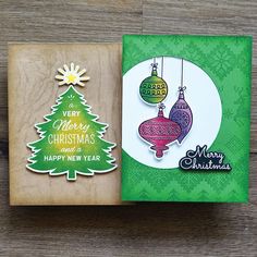 two christmas cards with ornaments on them sitting next to each other in front of a wooden background