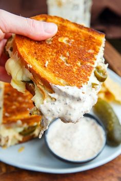 a person is holding up a grilled cheese sandwich with pickles and ranch dressing