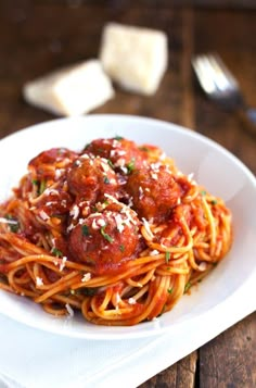 a plate of spaghetti with meatballs and parmesan cheese on top, ready to be eaten