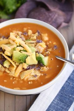 a white bowl filled with soup and topped with avocado, tortilla chips