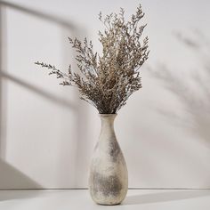 a vase filled with dried flowers on top of a white tablecloth covered floor next to a wall