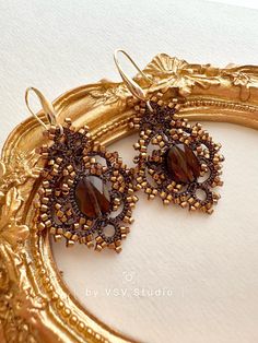 a pair of gold earrings with brown stones on them sitting in front of a mirror