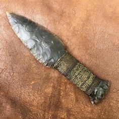 a knife that is on top of a brown leather surface with some dirt around it