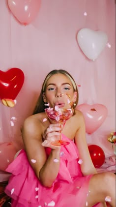 a woman in a pink dress sitting on a bed with balloons and confetti