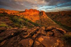 the sun is setting over some rocks in the desert with grass and bushes growing on them