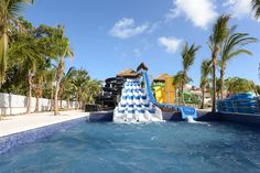 a water slide in the middle of a swimming pool surrounded by palm trees and blue skies