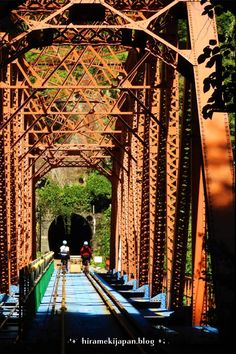 two people are standing on the side of a train track under an old metal bridge