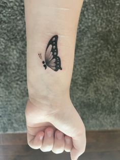 a small black butterfly tattoo on the left inner arm and wrist, with dots in it's wings