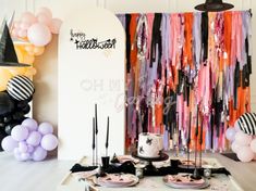 a table topped with cake and balloons next to a halloween themed wall hanging from the ceiling