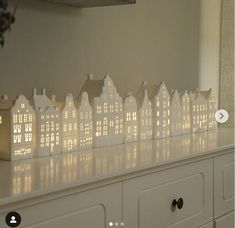 a white dresser topped with lots of small houses next to a window covered in lights