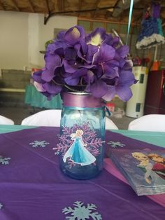 purple flowers are in a mason jar on a table with snowflakes and frozen princess pictures