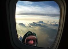 an airplane window with a person sticking their tongue out and clouds in the sky as seen from inside