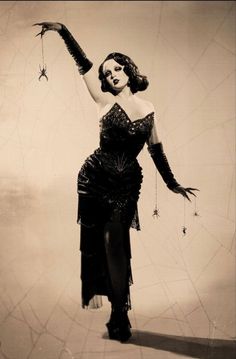 a woman in a black dress is holding a spider on her arm and posing for the camera