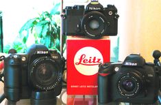 three cameras sitting on top of a table next to a box with the logo of a brand