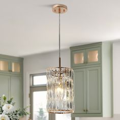 a chandelier hanging from the ceiling in a kitchen with green cabinets and white flowers