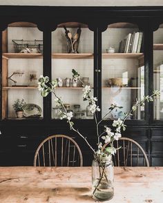 a vase with flowers sitting on top of a wooden table in front of a china cabinet