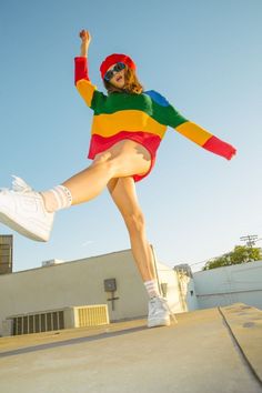 a woman in a colorful shirt and skirt is doing a trick on a skateboard