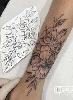 a woman's arm with flowers on it and a piece of paper next to her