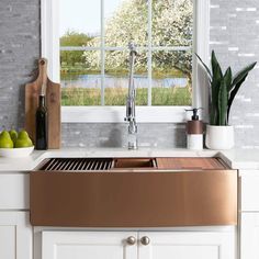 a kitchen sink sitting under a window next to green apples