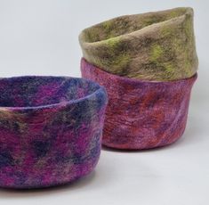 three different colored bowls sitting next to each other on a white surface with one purple and one green