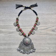 This Kuchi pendant necklace is the perfect statement piece and the perfect addition to your collection.  The large Kuchi pendant has uniform hand hammered designs and the centre is inlaid with red and green glass stones.  Hanging from the pendant are chains with diamond-shaped gilt pieces that make beautiful noise with movement.  The unique part of this necklace is the chain is made of round red and black cotton balls and large vintage coins.  This piece is from the 1980's and has some patina bu Kuchi Jewelry, Round Pendant Necklace, Round Pendant, Black Cotton, Diamond Shapes, Patina, Statement Pieces, Jewelry Box, Jewelry Necklace Pendant