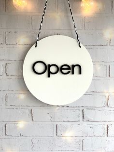 an open sign hanging on a brick wall with lights around it and the word'open'written in black