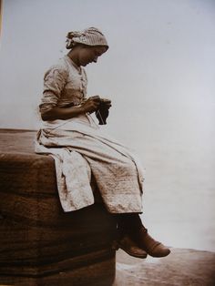 an old photo of a woman sitting on top of a wooden box looking at her cell phone