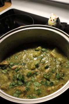 a pot filled with green food sitting on top of a stove next to a cat figurine