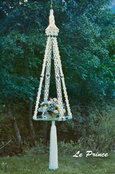 a white crocheted pole with flowers on it in front of some trees and bushes