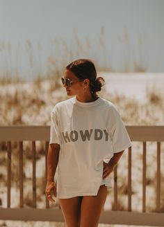 a woman in white shirt and shorts walking on the beach