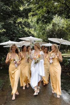 a group of bridesmaids walking in the rain with umbrellas