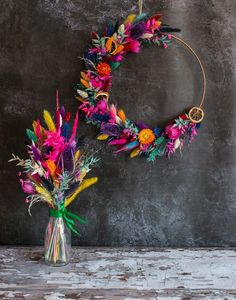 two vases filled with colorful flowers on top of a wooden table next to a gray wall