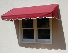 a red awning on the side of a white building with two windows in it