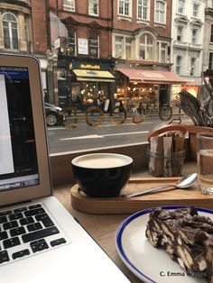 a laptop computer sitting on top of a wooden table next to a plate of food