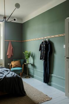 a bed room with a neatly made bed and clothes hanging on a rail next to a chair