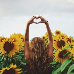 a woman standing in a field of sunflowers making a heart shape with her hands