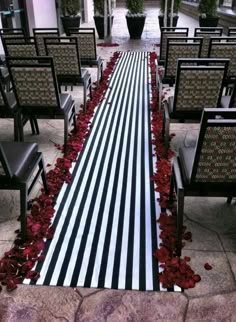 the aisle is decorated with black and white striped fabric, red rose petals, and greenery